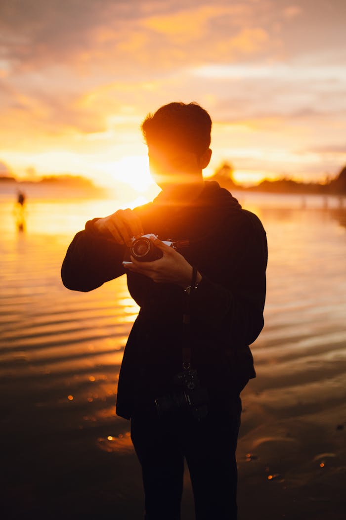 Silhouette of a photographer holding a camera at sunset on a beach.